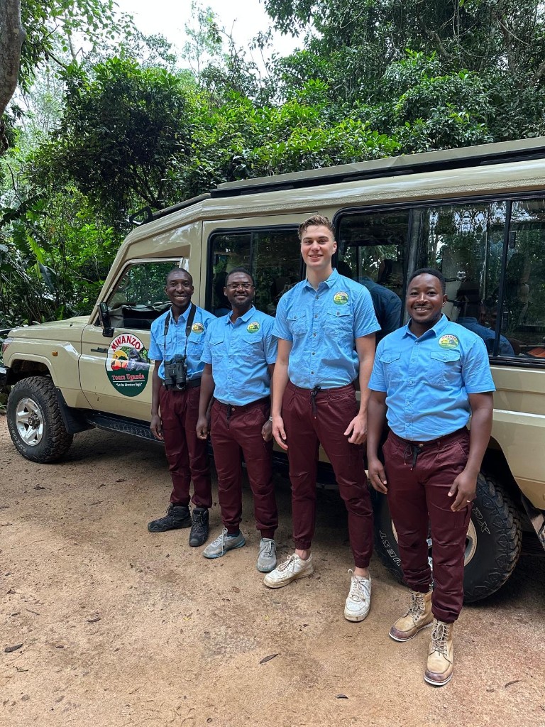 Four Mwanzo Tours guides in uniform beside a branded safari vehicle
